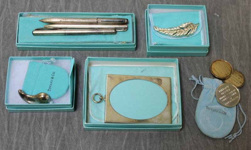 STERLING. Tiffany & Co. Group.: Includes a sterling frame, 3 pens, $225 in Tiffany gift coins, an Elsa Peretti brooch, and a Peretti feather form brooch. Total approximate weight of 2 brooches and gift coins is 3.29 troy oz. From a