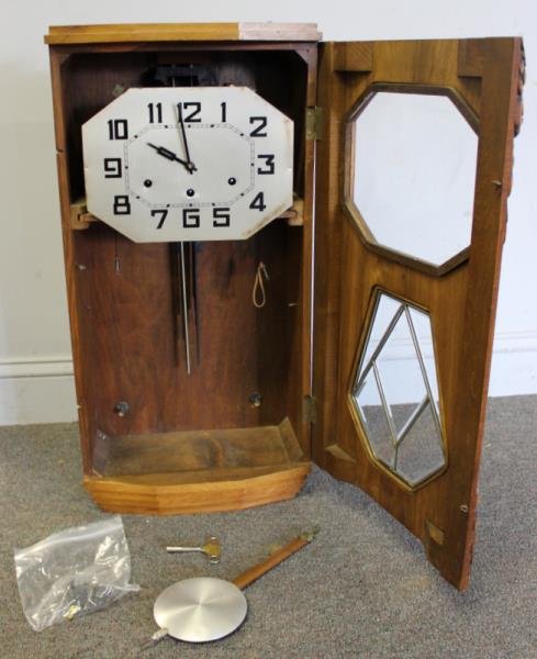 Art Deco Wall Clock.: Carved case with lower beveled glass door. With time and chime strike; key and pendulum. From a Nyack, NY estate. Dimensions: 13.5" w x 6.5" d x 27" h. Condition: Good, was running in house but all cl