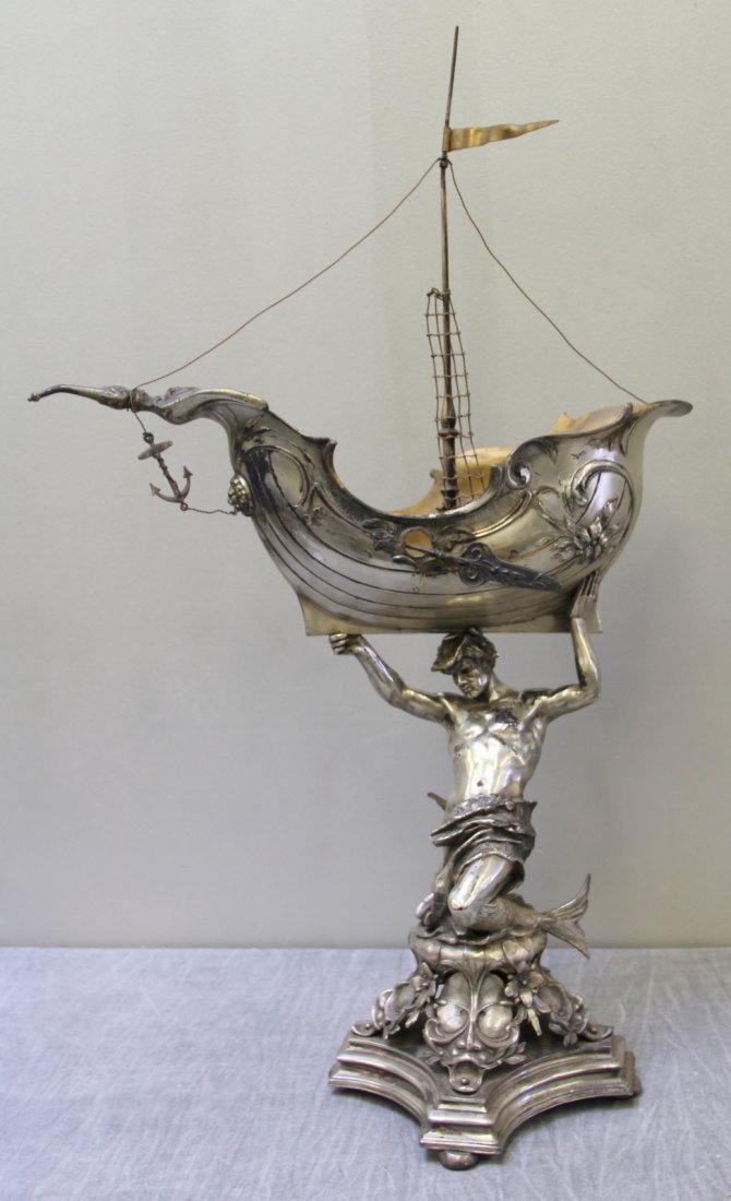 Large and Impressive Centerpiece of a Merman: Holding up a Nef Ship. Merman with upraised arms carrying a beautiful Nef ship on a pedestal base with floral and mask design. Apparently unmarked. From a Manhattan, NY estate. Dimensions: 18.875" w x
