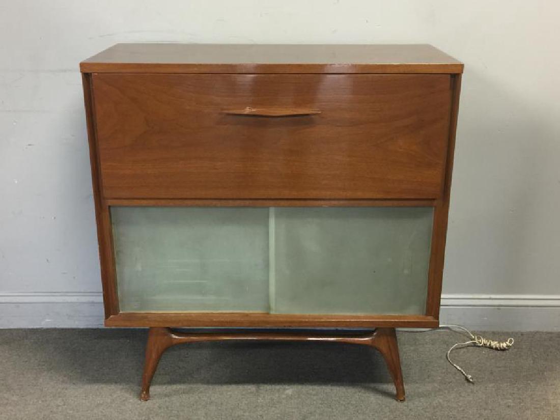 Midcentury Drop Front Bar Cabinet.: Interior fitted with cirucular cut-out shelf and light with mirrored back. Sculpted base and slide front glass door lower shelf. From a Manhattan, NY estate.