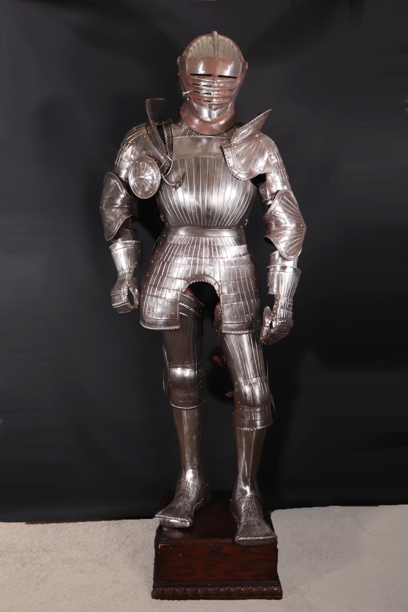 'Maximilian-Style' Suit of Armour: Composed Jousting Maximilian Armour of the 15th century-style. Steel, brass, leather, cloth.Very well mounted harness on full mannequin of early hardwood base and dark wood color. Helm consisting of b