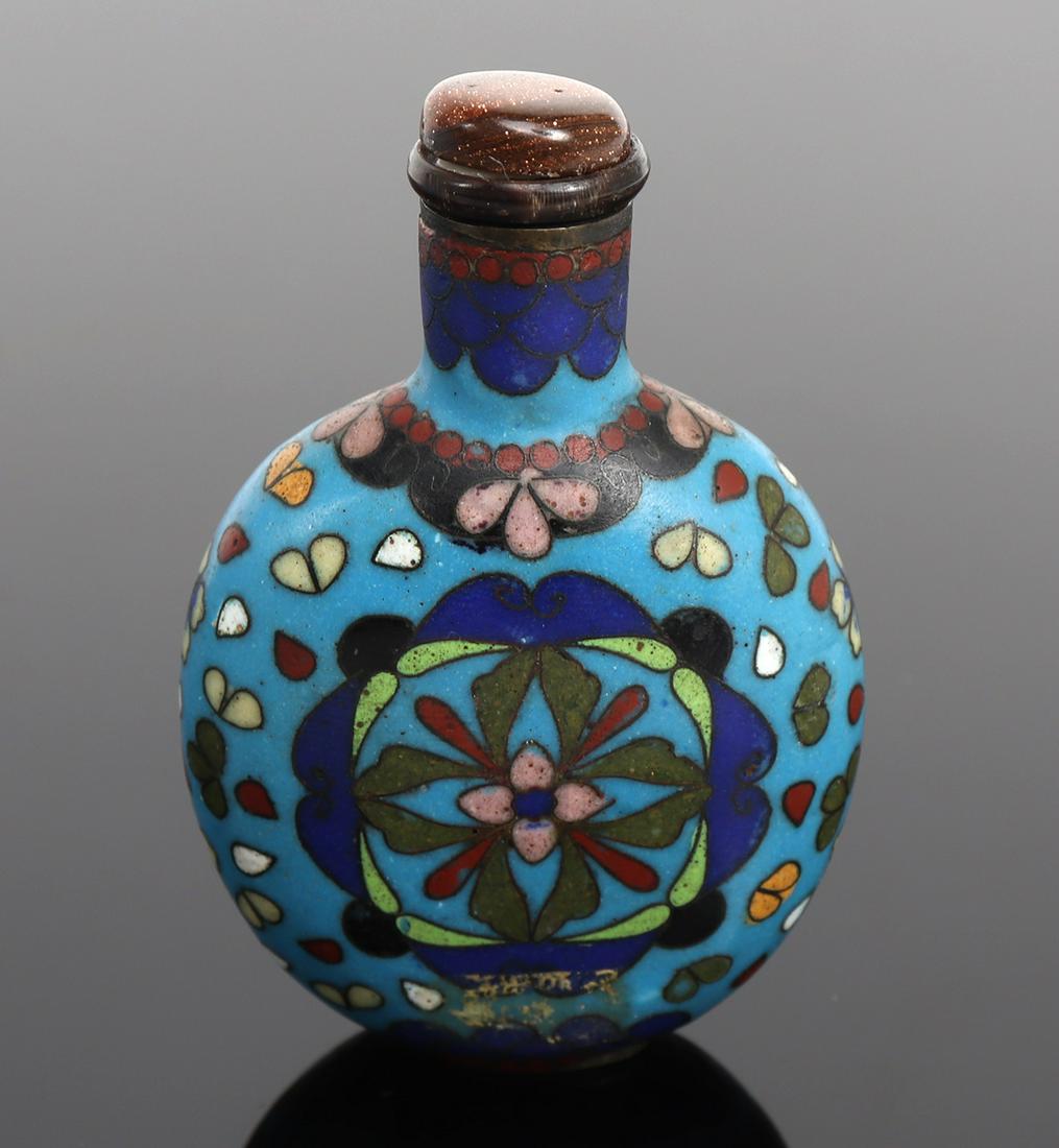 Chinese Cloisonne Snuff Bottle: Antique Chinese cloisonne snuff bottle, blue background with light greens, pinks and blue hues throughout. Floral and leaf detail to each side. Stopper is a hardstone with sparkles that glisten in nat