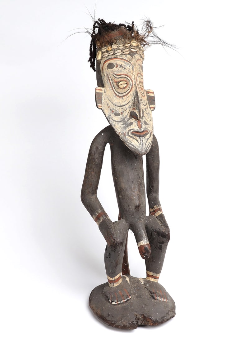 Papua New Guinea, 20th Century Spirit Figure: Tall PNG spirit figure carved out of wood with pigment, cowrie shells, fiber, fur and feathers. The spirit figure appears to be leaned against a painted stool, with his phallus exposed and painted. Th