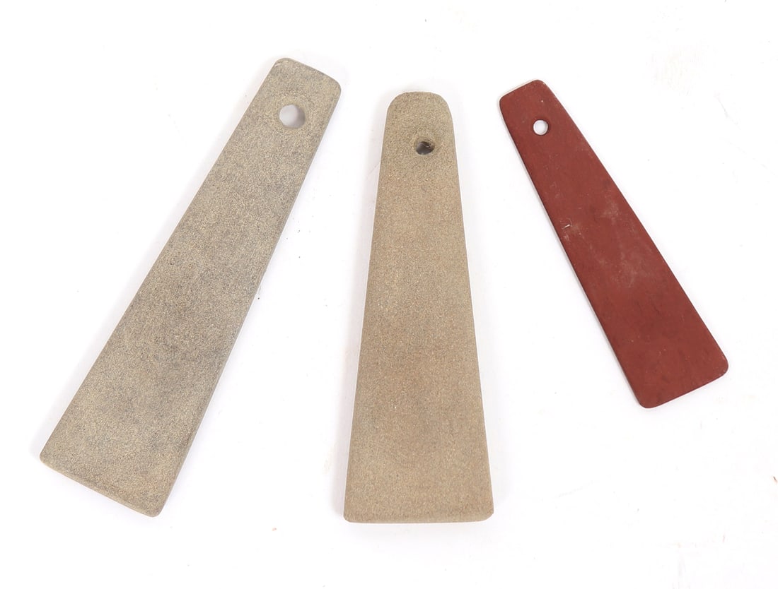 Three Native American Stone Gorget Pendants: Group of three Native American stone gorgets pendants. Two have a soft cream color, the third a vivid red stone. Each gorget features conically drilled holes. Size of largest 5" L