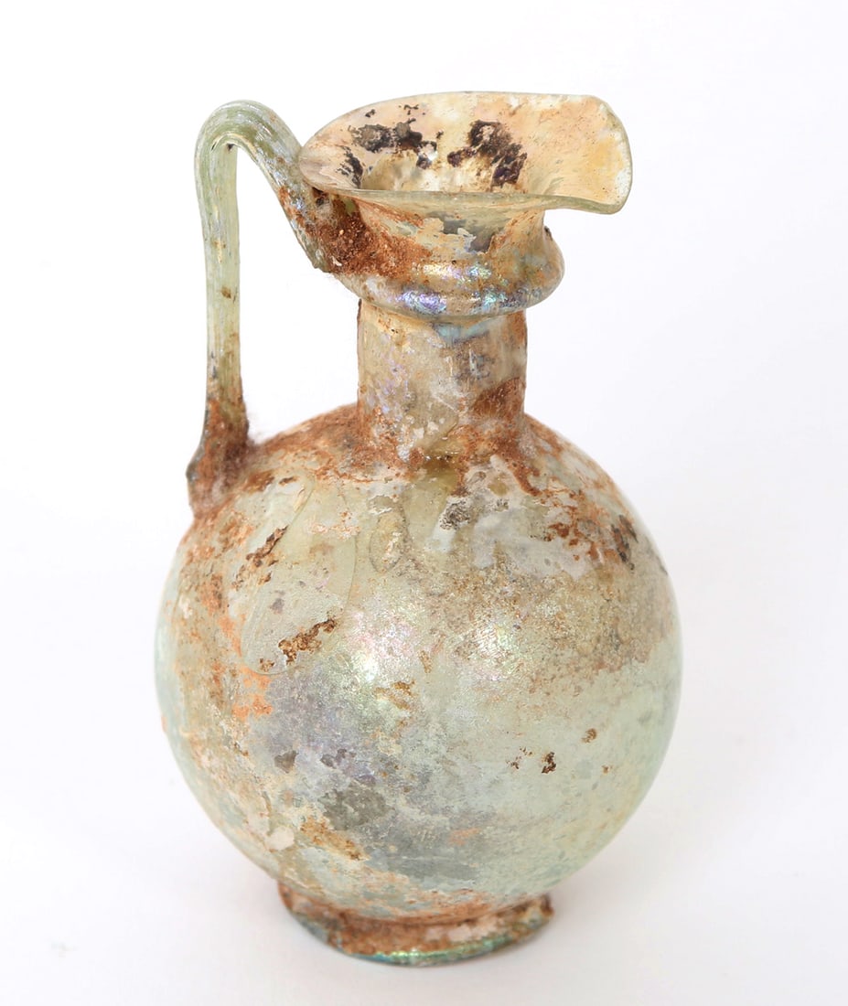 Roman Green Glass Trefoil Oinochoe, 2nd-3rd AD: Lovely green glass blown vessel with bulbous chamber, cylindrical neck with ring of applied trailing. Look handle and trefoil shaped pouring spout. Size 3 1/4" H. For other similar examples see Shinni