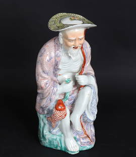 'Happy Fisherman' Figural Porcelain, Republic Period or Earlier: Chinese Porcelain sculpture of a Happy Fisherman seated atop a colorful green base, wearing a light peach robe with specks of red stippling and blue Chinese characters in bands, the fisherman can be s