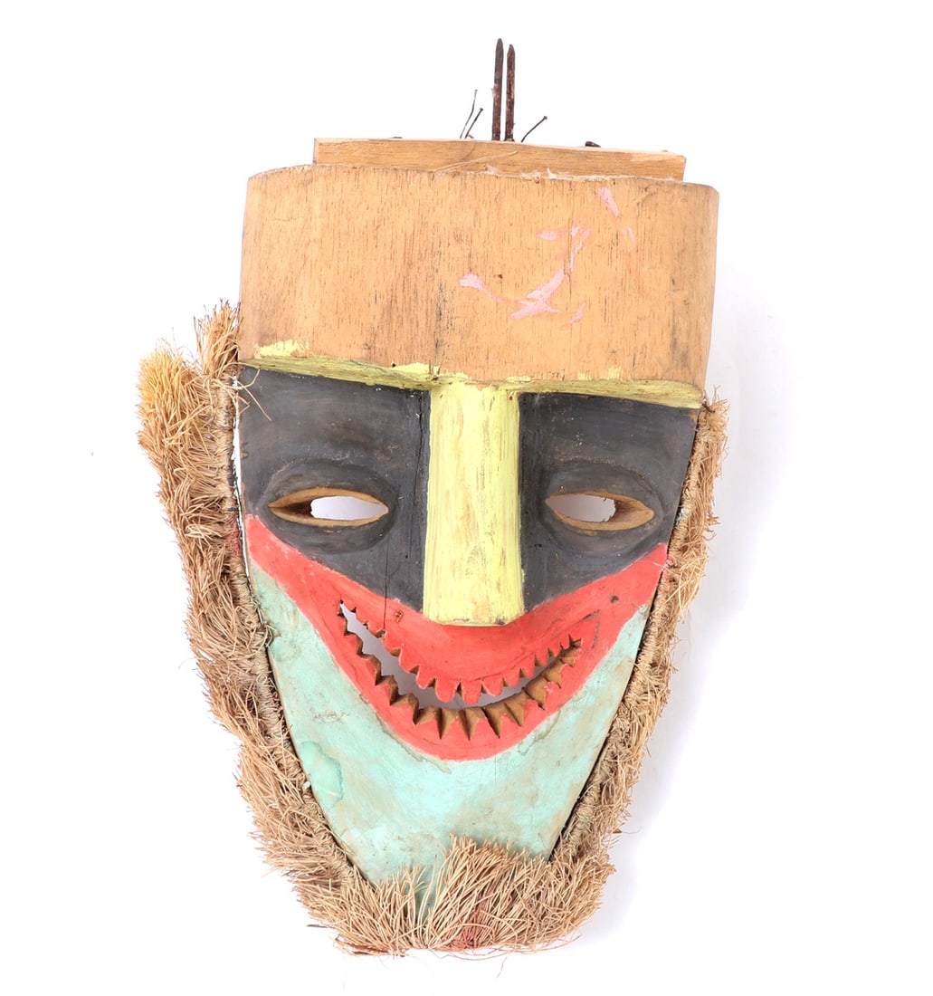 Tolai People Brightly Painted Wood Carved Mask: New Britain, Gazelle Peninsula Tolai wood carved mask with a long chin beneath a smiling mouth with carved teeth, the nose wedge shaped below a heavy brow. Yellow, black, red and turquoise colored pig