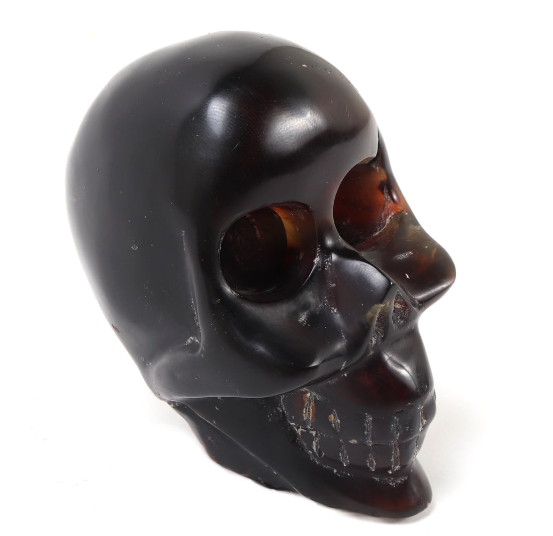 Fossilized Amber Carved Skull: Fine section of ancient fossilized amber, wonderfully crafted into an intimidating human skull. Wide deep socketed eyes, high cheek bones and big toothy grin. Size 4" H x 2 1/8" W
