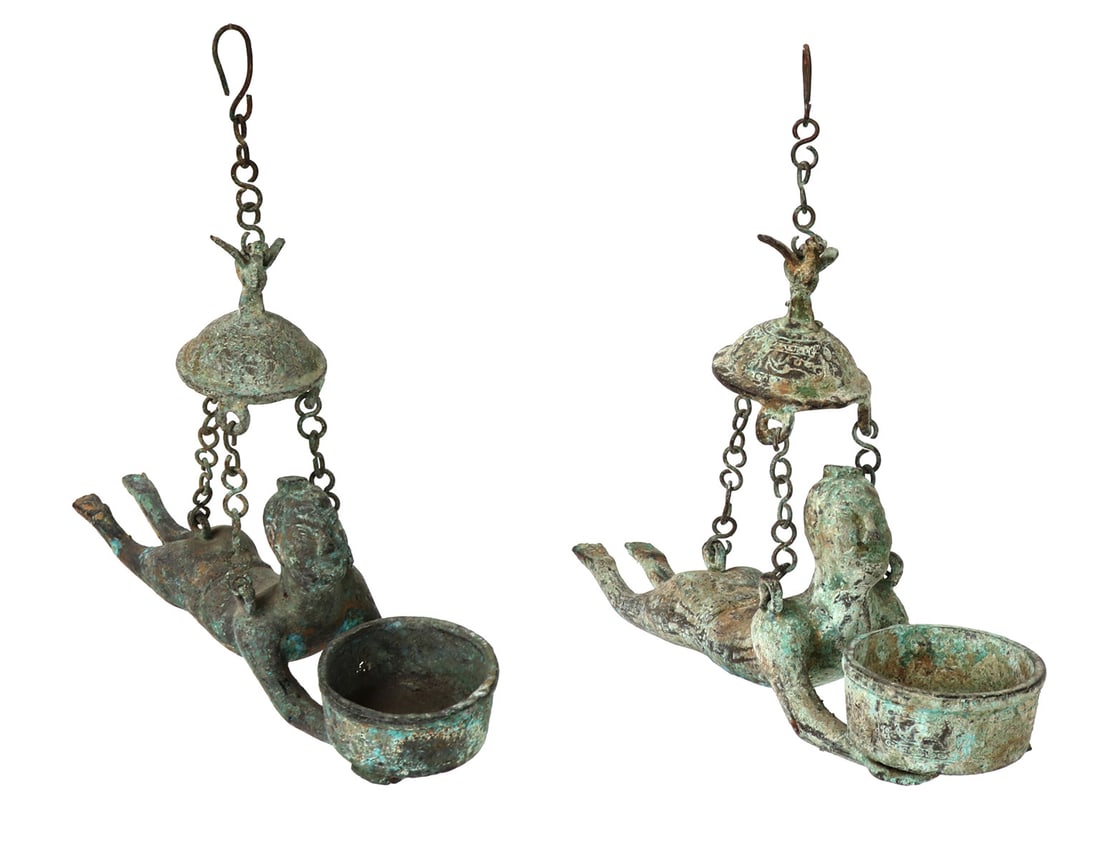 Two Suspended Chinese Bronze Oil Lamps: Fine pair of Chinese bronze oil lamps. Each depicting a man laying out as though in flight while holding a bowl for oil. Each suspended by three chains affixed to the back. Surmounted with a incised c