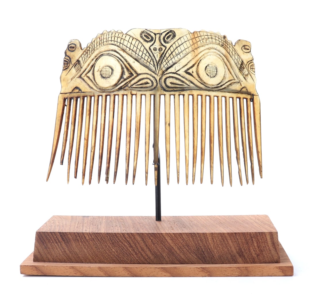 Tiki Face Bone Carved Comb with Stand: Handsome and well detailed bone or shell carved comb, incised details to the top make up of a tiki style face with zoomorphic faces to the center as well as to the sides. Several individual comb