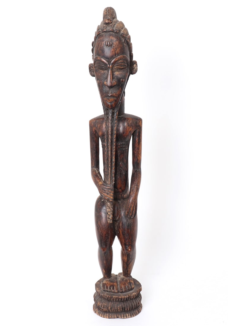 Standing Male Spirit Figure, Baule: West Africa, Ivory Coast, Baule peoples statue of a standing male ancestor. Dark brown wood patination. Figure with one hand holding a long braided beard. Scarification throughout the body. Slightly