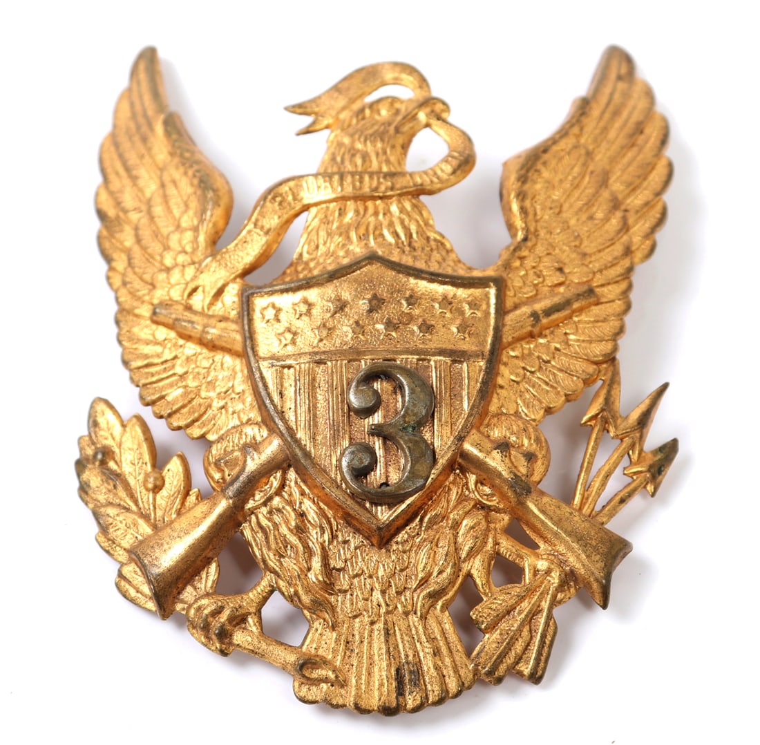 Early Brass Helmet Badge, Great Seal of the United States: Indian War US Army artillery dress helmet plate with an eagle soaring with a ribbon reading - E Pluribus Unum hanging from his beak. Crossed rifles behind a the ranking badge marked 3, with arrows and