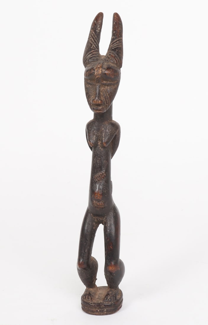 African Dan Wood Carved Woman: Late 19th to early 20th century, hand carved wood standing figure. The woman presents with her arms crossed behind her back and is wearing a traditional Dan style mask with horns. Her belly has hash