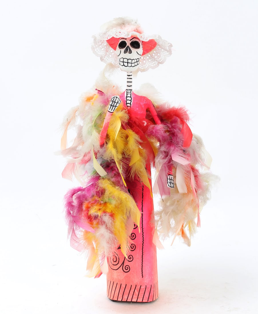 Dia De Los Muertos Paper Mache Cartina Doll: Elegantly dressed Catrina doll of a female skeletal figure wearing a large white lace trim and pink hat. Adorning a large pink and multicolored feather boa over a long pink dress with black linear