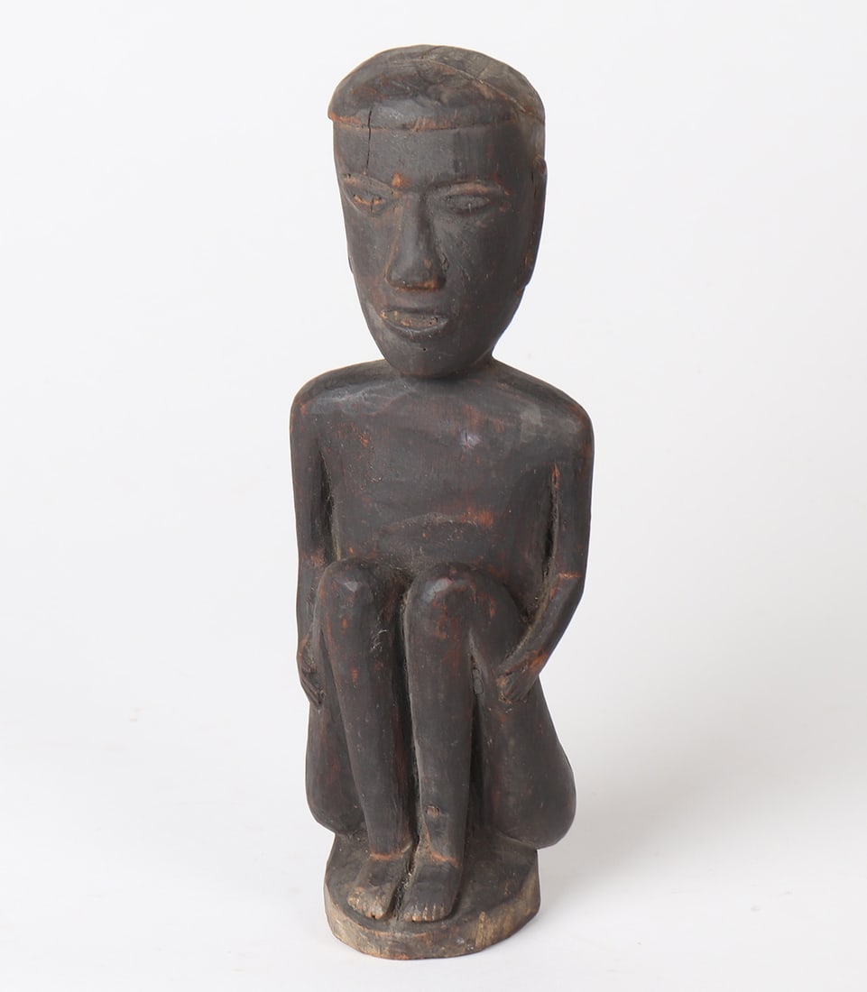 Seated Bulul Wood Carved Statue: Uniquely carved in a much more human form that normal, the figure sits with knees to chest, and hand on his thighs. His mouth is open, with almond eyes, and bell shaped nose. The Bulul is covered in