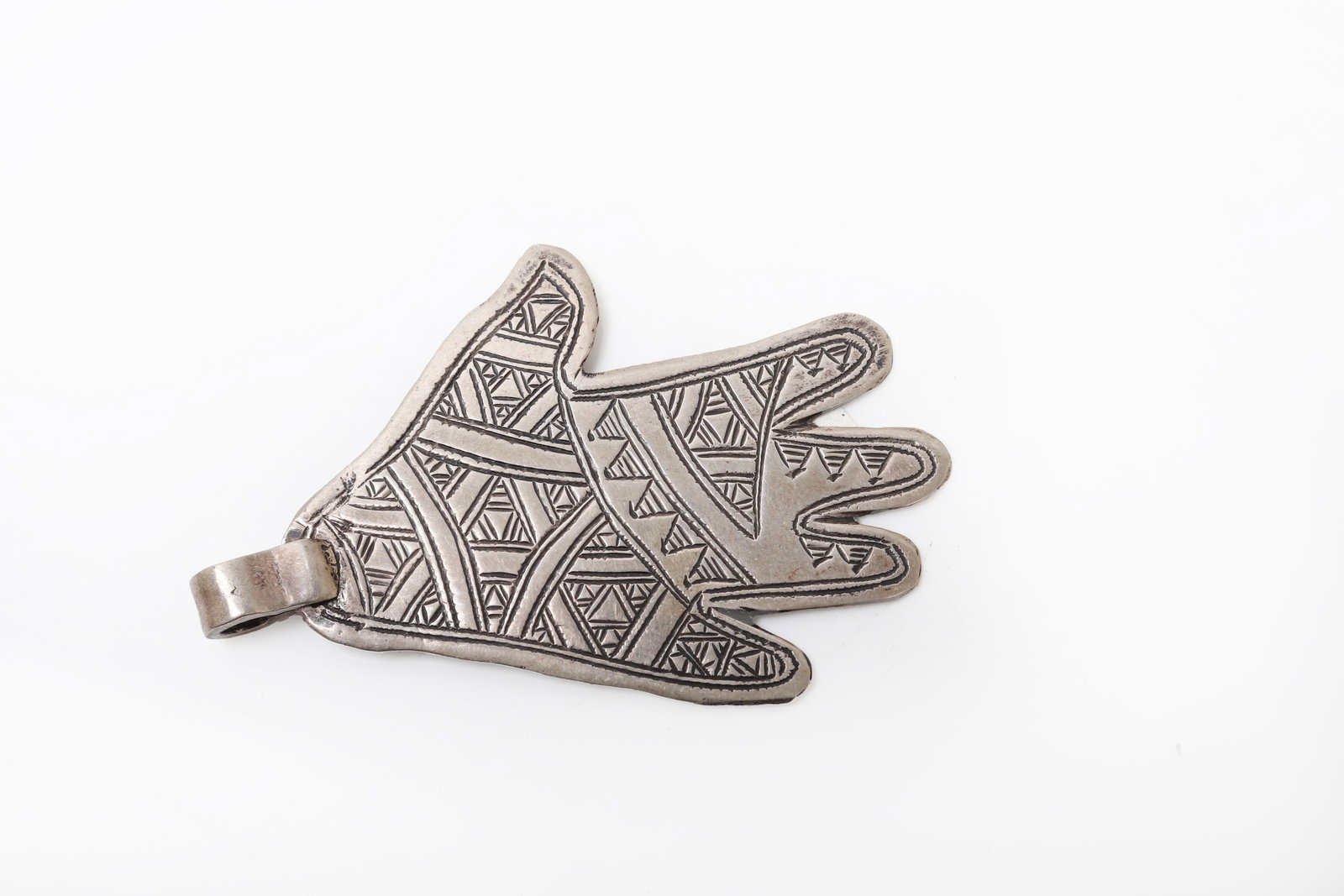 Moroccan Silver Khamsa Hand Pendant: Morocco, 19th to early 20th century. Silver pendant in the form of a stylized hand, engraved throughout with geometric and linear ornament. The broad flat form and suspension loop suggest use as a
