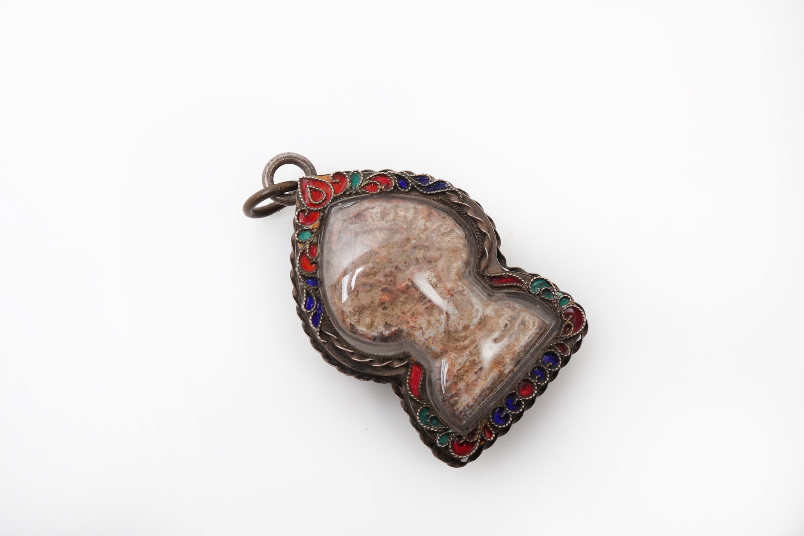 Thai Buddhist Amulet in Silver Enamel Mount: Thailand, 20th century A finely presented Thai Buddhist amulet of traditional form, the central sacred tablet enclosed within an ornate metal casing decorated along the border with delicate red,
