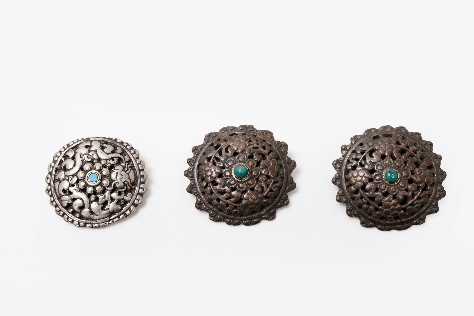 GROUP OF THREE BHUTAN ORNAMENTAL METAL DRESS ACCESSORIES: Bhutan shawl broches, early 20th century Three circular metal brooches known as a koma , each worked in openwork and relief with intricate filigree-like scrolls and floral-inspired motifs arranged