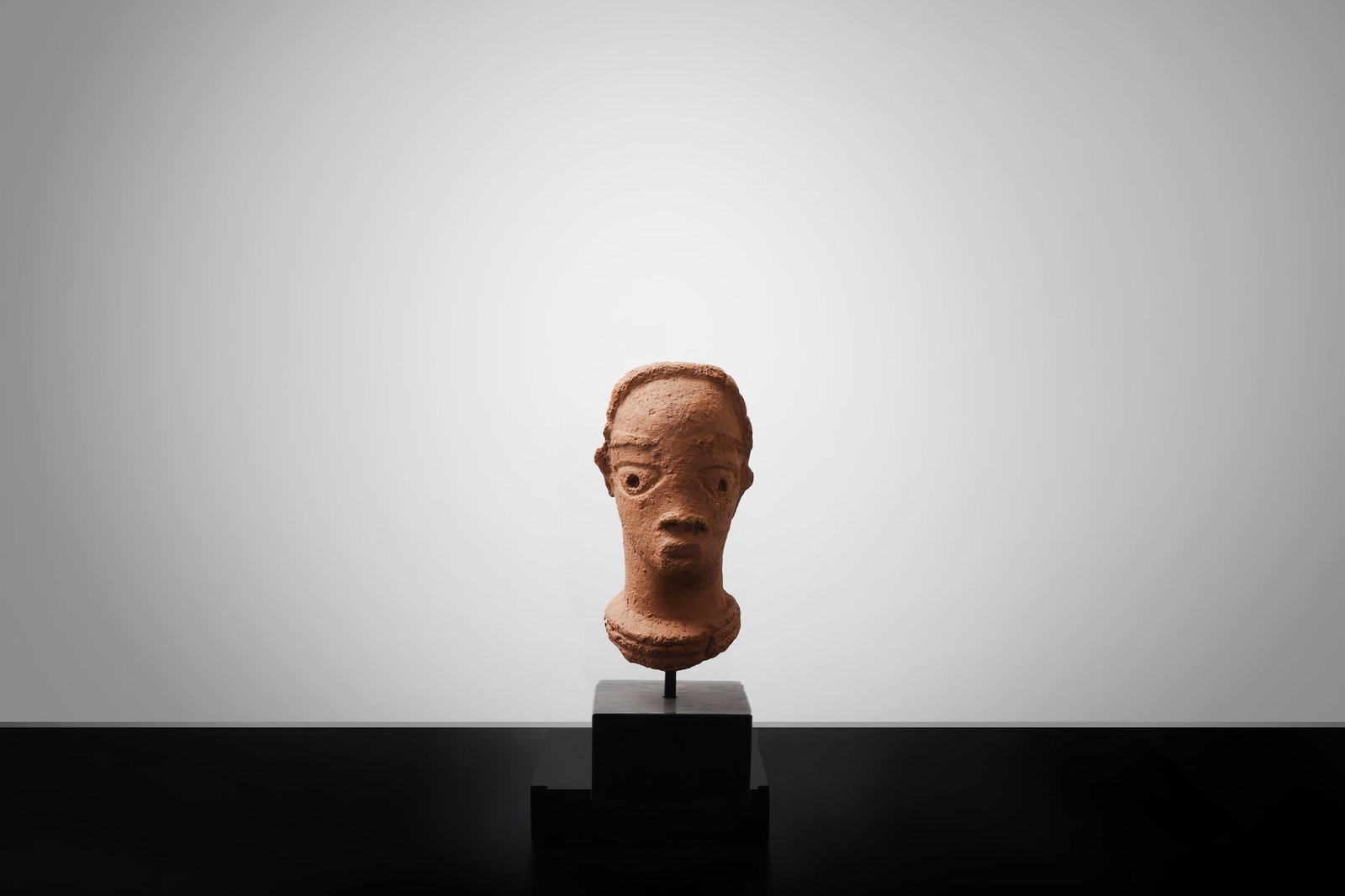 Nok Terracotta Head, 500BCE-200CE: West Africa, probably Nigeria, Nok culture, circa 500 BCE ? 200 CE. A finely modeled terracotta head, probably Nok, of elongated cylindrical form, with deeply recessed almond-shaped eyes, a long