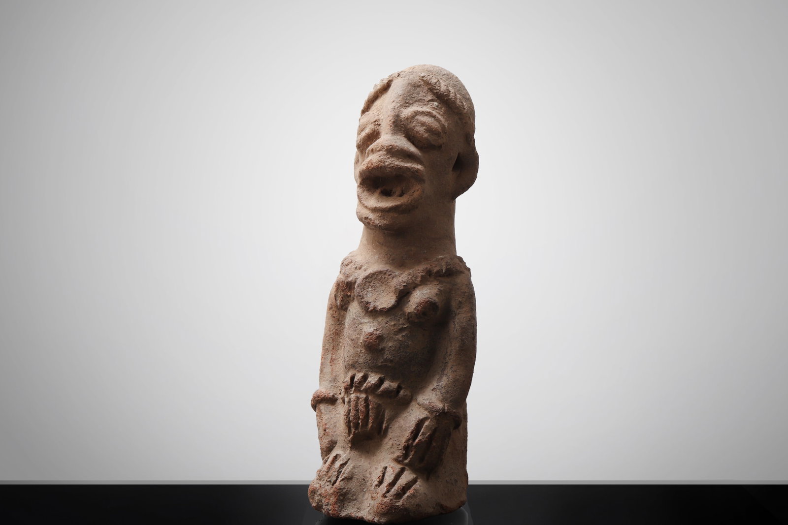 African Koma style Terracotta Funerary Figure: West African style terracotta female funerary figure. A modeled terracotta standing female figure, rendered in a distinctly archaic and expressive manner. The elongated head is surmounted by a subtly