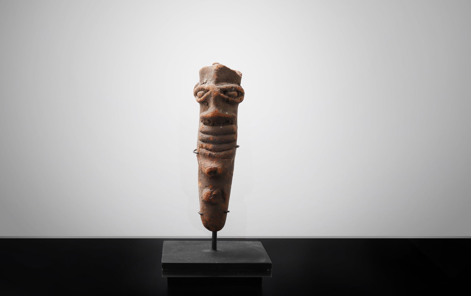 Terracotta Figure Fragment: West Africa, Possibly 1000 BE to 300 CE. Terracotta figural fragment of elongated tapering form, surmounted by a stylized head with prominent brow, projecting nose, and deeply modeled mouth above a