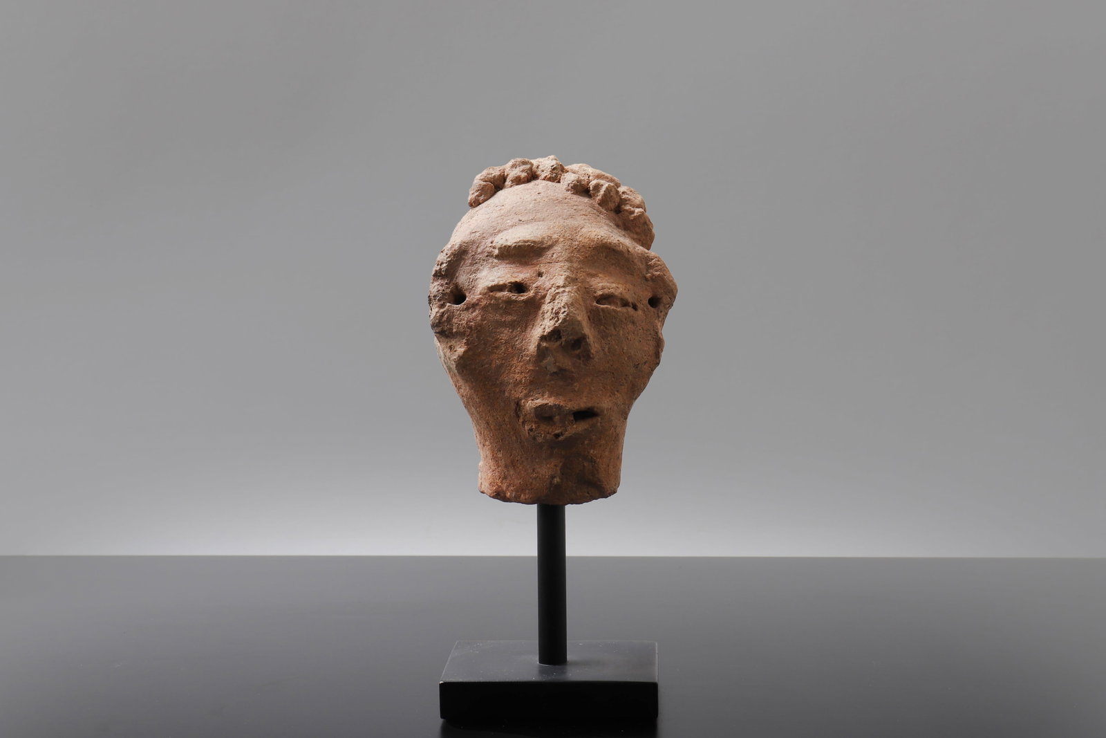 African Terracotta Male Head: Africa, style of West African terracotta circa 500 BE to 200 CE . Terracotta head fragment with sensitively modeled features, including narrow slit eyes, a broad nose, parted mouth, and a textured