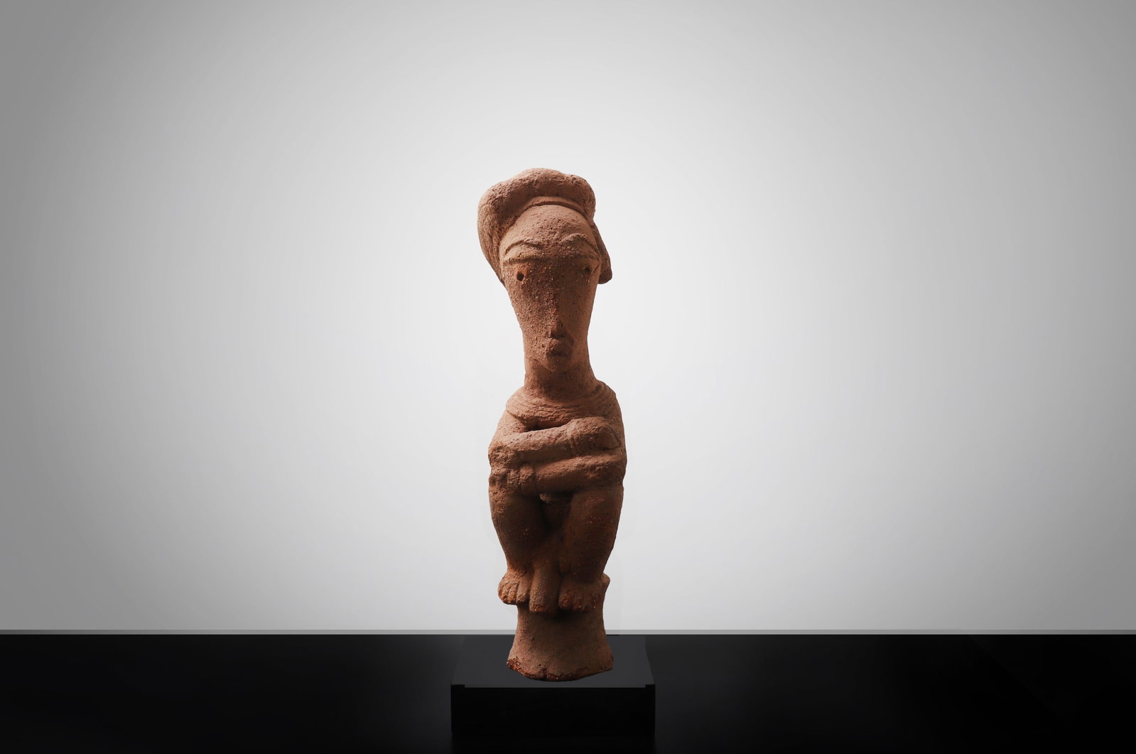 Nok-Style Terracotta Seated Figure: West Africa, Nigeria, Nok culture or Nok style, possibly 500BCE - 200CE. A terracotta seated figure modeled in reddish earthenware, shown with knees drawn upward and arms folded across the front of th