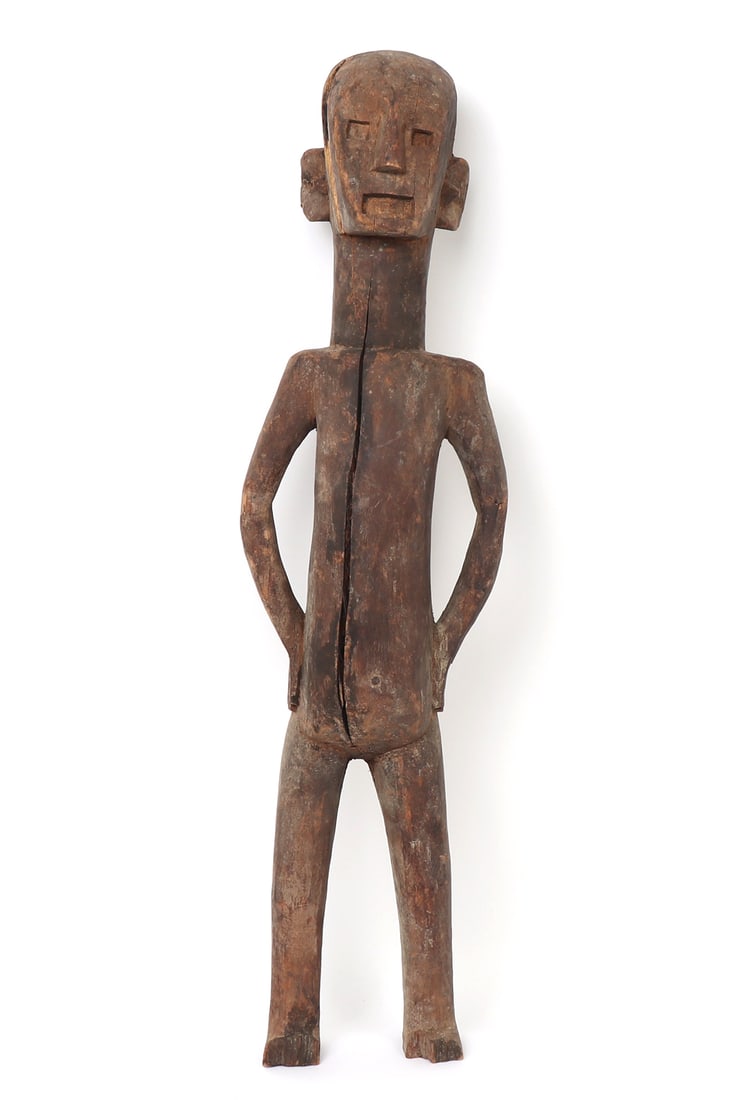 Sukuma Male Figure: Africa, Tanzania, Sukuma peoples, 20th century. Carved wood standing male figure, the elongated body with squared shoulders, narrow waist, and arms bent with hands resting at the hips. The head is