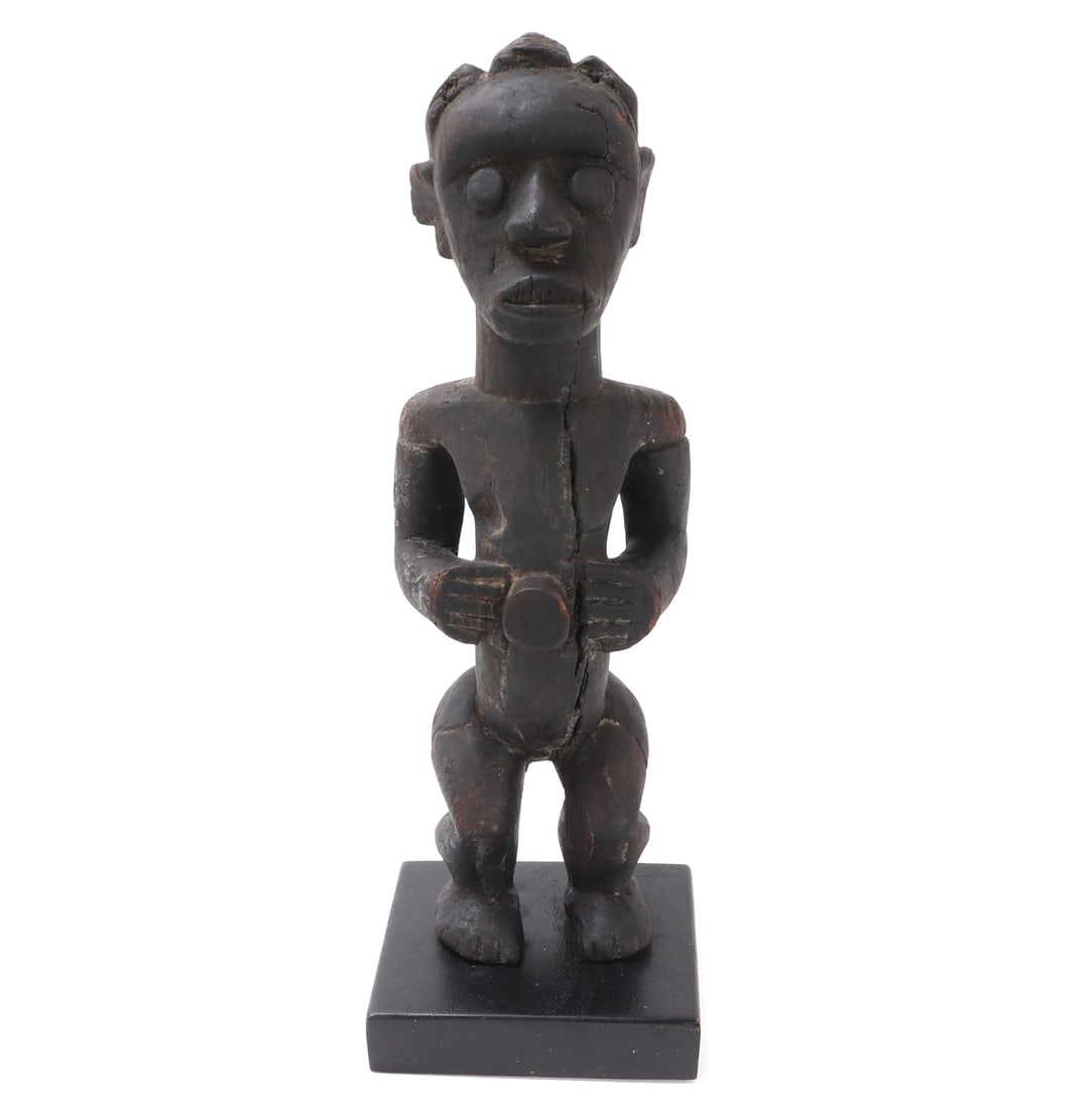Carved Wood Fetish Figure w/Stand: African wood carved fetish or reliquary figure with round protruding eyes, braided coiffure, triangular protruding nose. He stands with his hands at his belly where a 'button' is carved in high relief