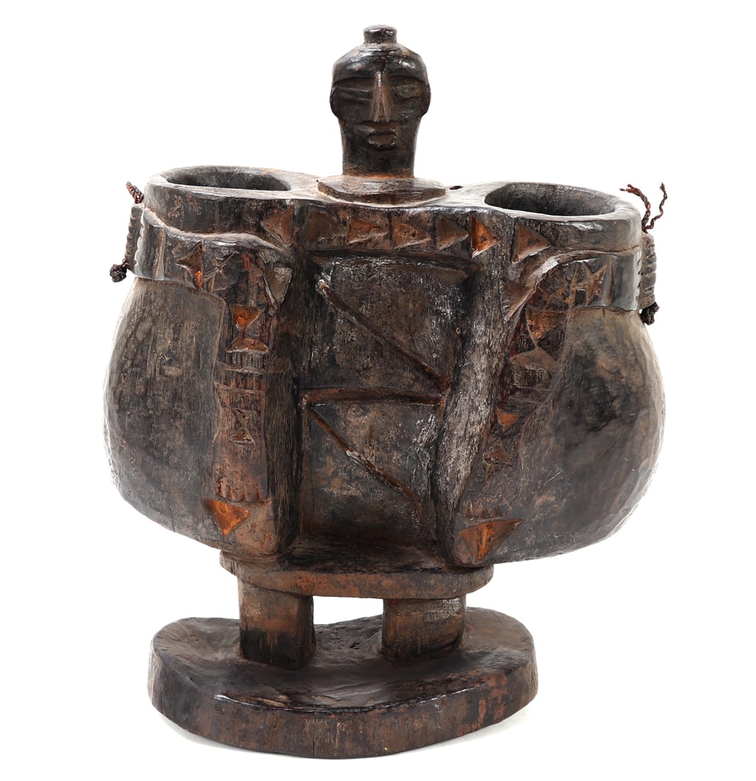 Carved African Double-Chamber Figural Vessel: Africa, probably West or Central Africa, early to mid-20th century A substantial carved wooden double-chamber vessel, skillfully hollowed from a single heavy piece of wood. The composition is formed