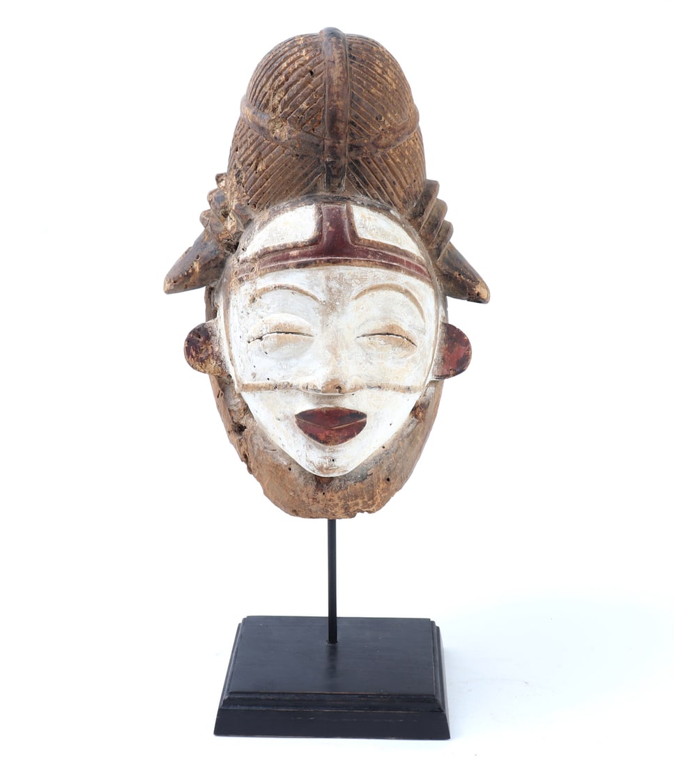 Punu White-Pigmented Wood Mask, Gabon: Gabon, Punu or Lumbo peoples, carved wood mask with white-pigmented face, red-painted lips, ears, and brow ornament, and an elaborate ridged coiffure rising above the forehead. The face is modeled