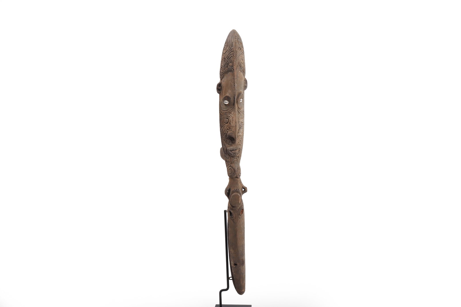 Papua New Guinea Carved Figural Canoe Ornament: Papua New Guinea, circa 1980s. Carved wood ornament of elongated vertical form, worked with a stylized ancestral face, pierced shell-inset eyes, and incised scrolling decoration. The attenuated lower