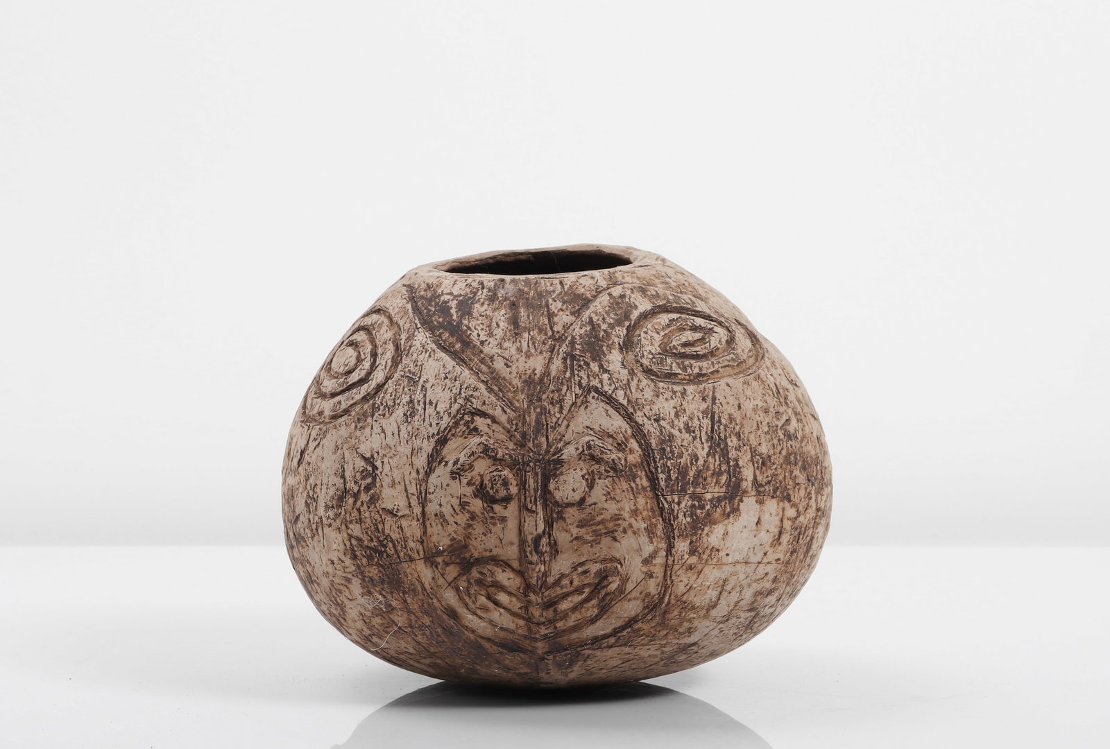Carved "Bemble" Coconut Shell Vessel: Probably Southeast Asia or the Pacific, 20th century. Carved coconut shell vessel of rounded form, incised on one side with a stylized face framed by curvilinear motifs and spiral devices. The