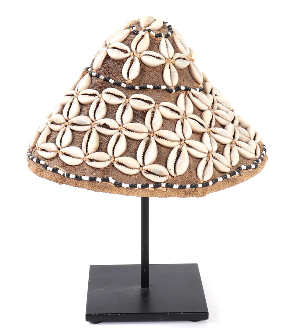 Kula Shell-Adorned Hat: Probably Papua New Guinea, 20th century or earlier. Conical woven fiber hat densely ornamented with cowrie shells arranged in radiating floral clusters, further accented by bands of black and white
