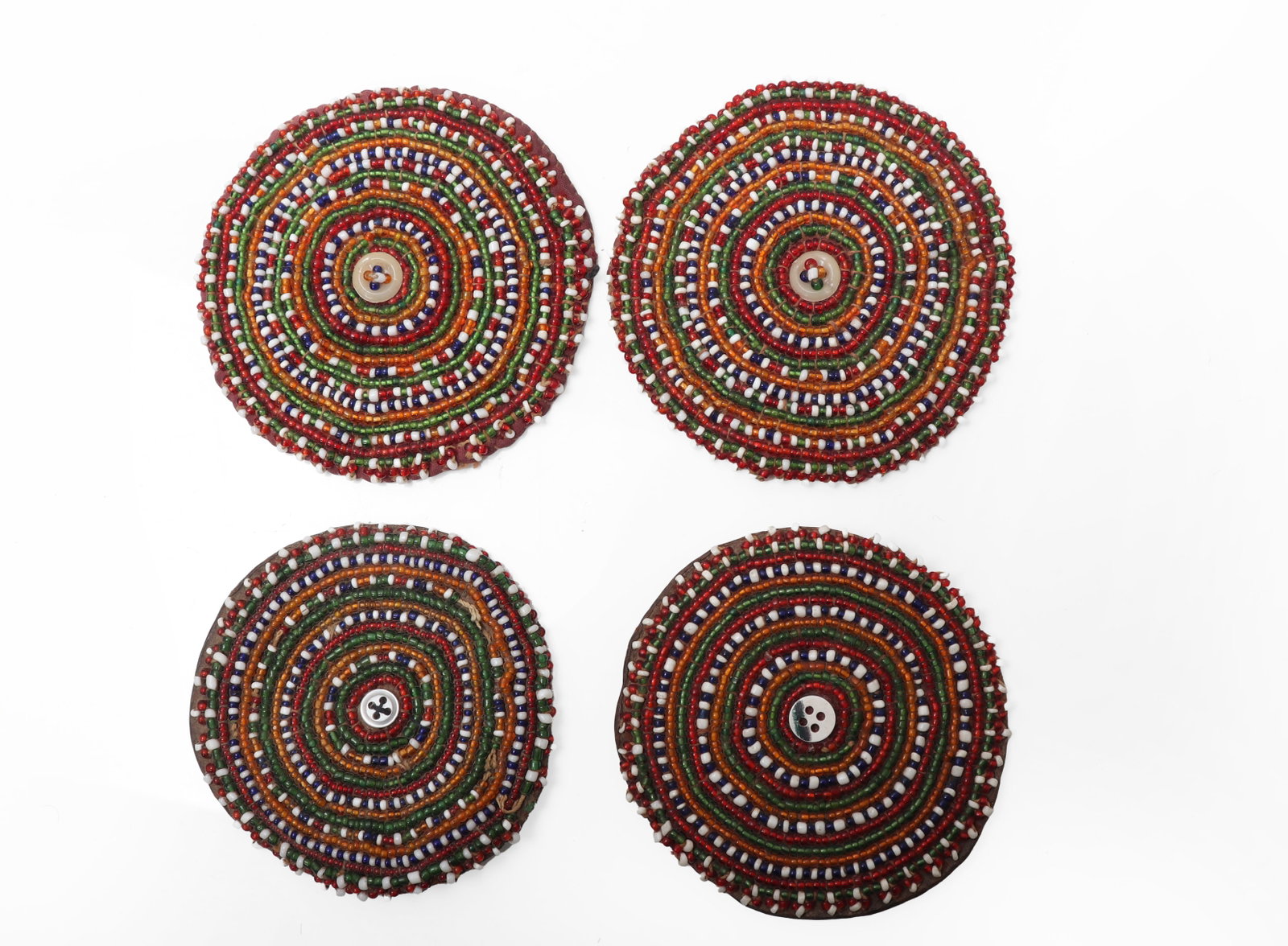 Set of Four Polychrome Beaded Covers: India, 19th to early 20th century Set of four circular beaded covers, each worked in concentric rings of polychrome glass seed beads in red, green, blue, white, and amber tones, centered by a small