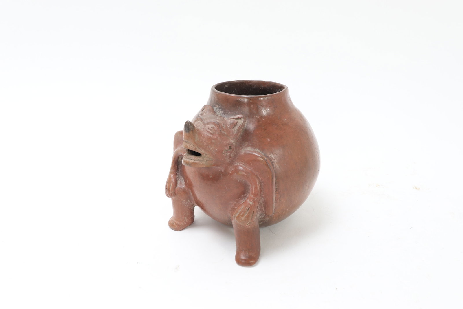 Pre-Columbian Maya-Style Ceramic Bat Effigy Vessel: Ceramic vessel of globular form on three supports, modeled with an applied bat-like deity or supernatural figure with projecting snout, upright ears, and folded limbs embracing the body. The