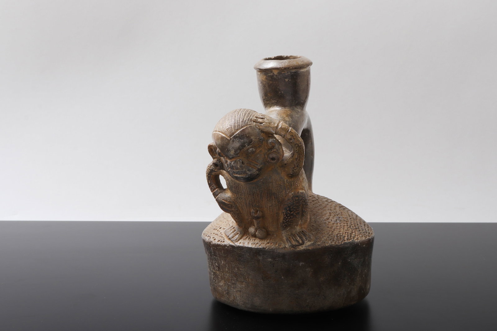 Pre-Columbian Style Stirrup Vessel: Pre-Columbian style monkey stirrup vessel, 20th century. Modeled after ancient Andean pottery forms. Ceramic vessel with arched stirrup handle, cylindrical spout, and applied crouching monkey figure