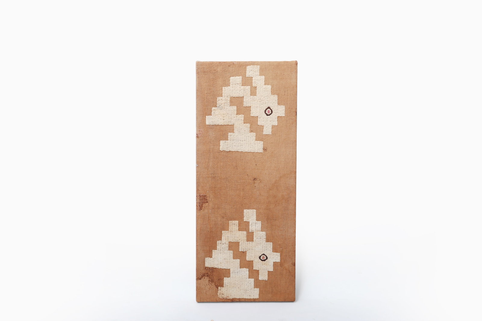 Pre-Columbian Avian Textile Panel Chancay 1000 - 1400 CE: A narrow woven textile panel of rectangular form, worked on a tan ground with two vertically arranged cream stepped geometric zoomorphic motifs, each centered with a small polychrome accent. The