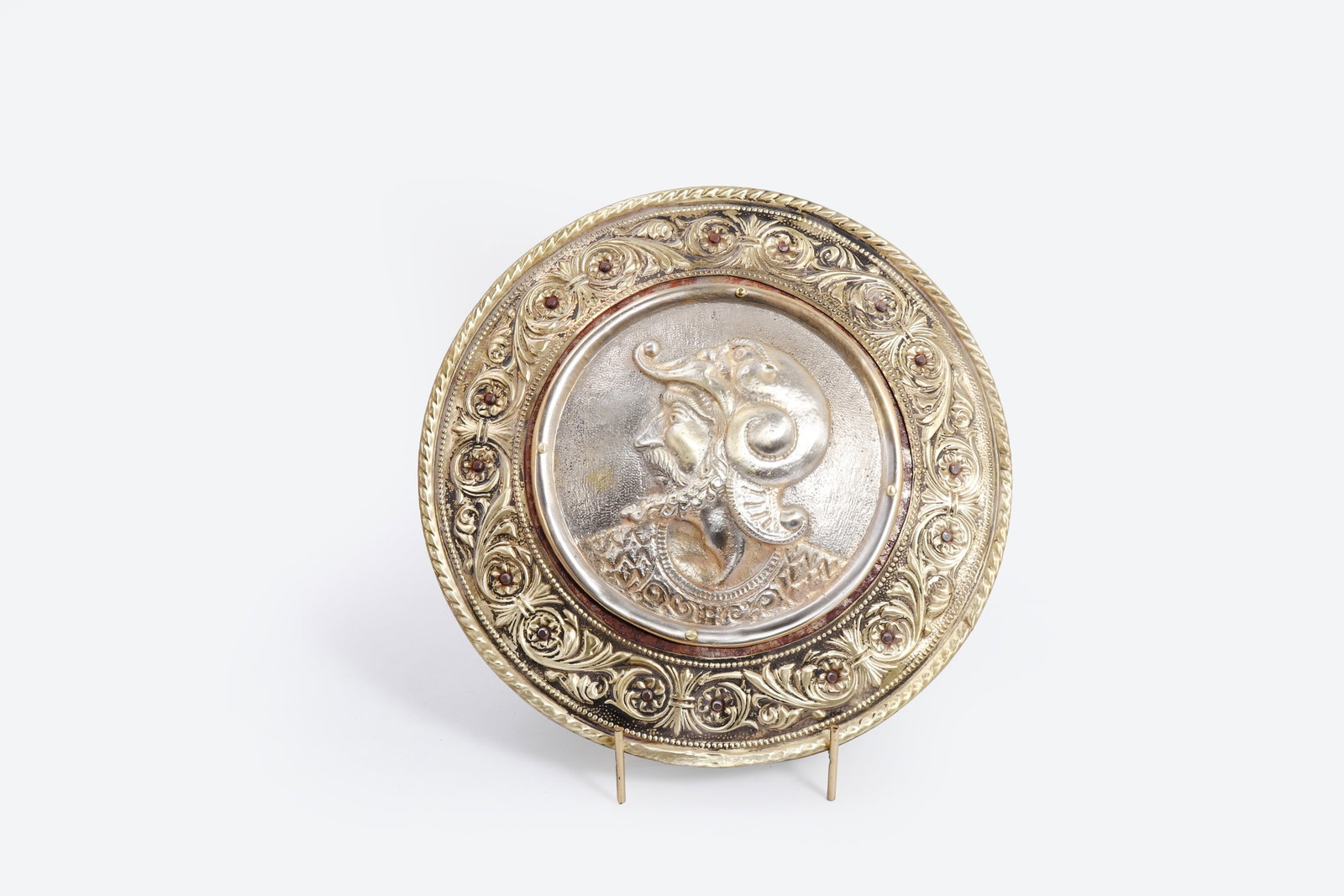Embossed Warrior Portrait Metal Plaque, 19th-20th C.: Continental European, possibly Spanish or Italian, likely late 19th to early 20th century. The circular plaque features a raised central profile portrait of a helmeted warrior or nobleman, surrounded