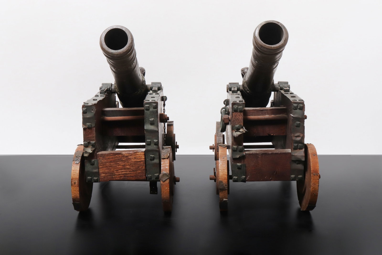 European Pair of Victorian Cannons: European, Victorian bronze model cannons, with tapering bronze barrels cast with raised ring bands, floral and scroll ornament, and heraldic style decoration. Each cannon is mounted on a wooden wheele