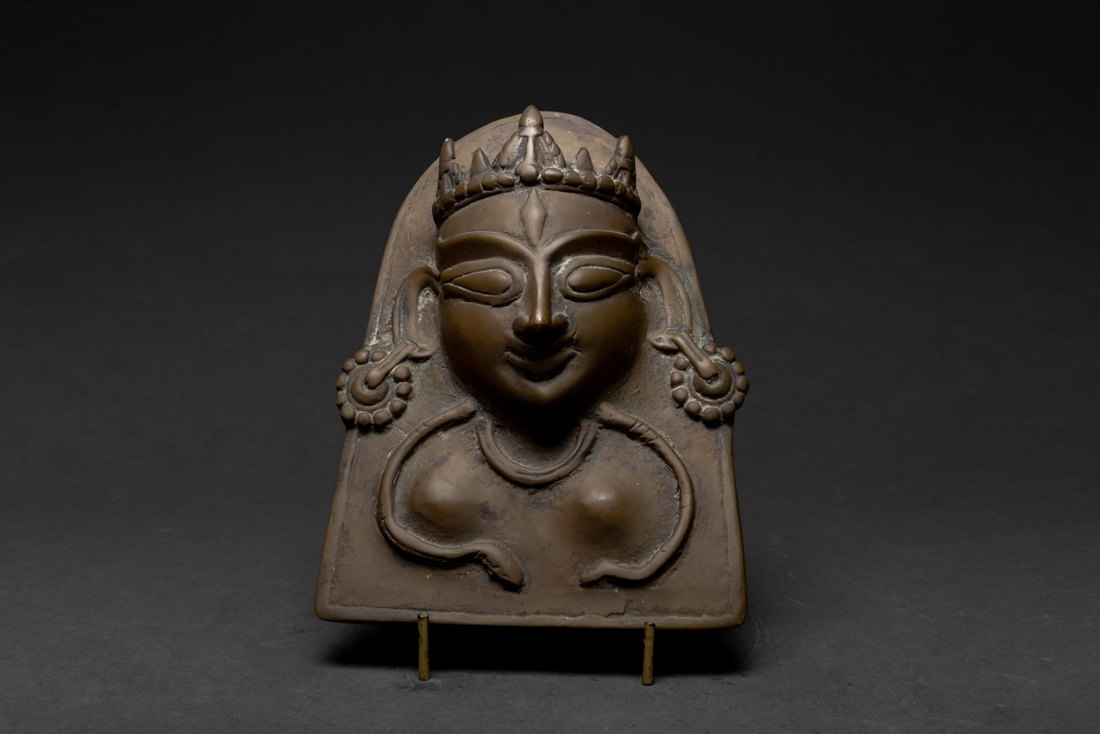 Indian Brass Shiva Plaque, 18th Century: 18th century Indian brass relief plaque depicting Shiva, shown with a crowned head, raised facial features, central forehead mark, large hoop earrings, and necklace detail. The arched plaque has a war