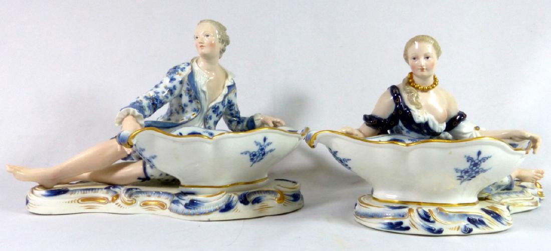 PR MEISSEN PORCELAIN FIGURAL SWEETMEAT DISHES: Pair of Meissen porcelain figural sweetmeat dishes in the blue onion pattern. Depict a semi-nude woman and man in blue and white with gold gilt accents. Crossed swords mark to underside. Female measur