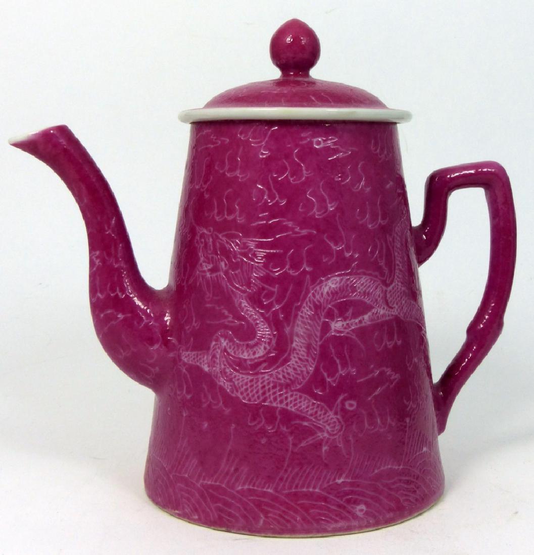 CHINESE PINK GLAZED PORCELAIN DRAGON TEAPOT: Chinese pink glazed porcelain lidded teapot with embossed scene of flaming dragons in the clouds. Holds six character calligraphy mark to underside. Measures 5 7/8" (15cm) height.