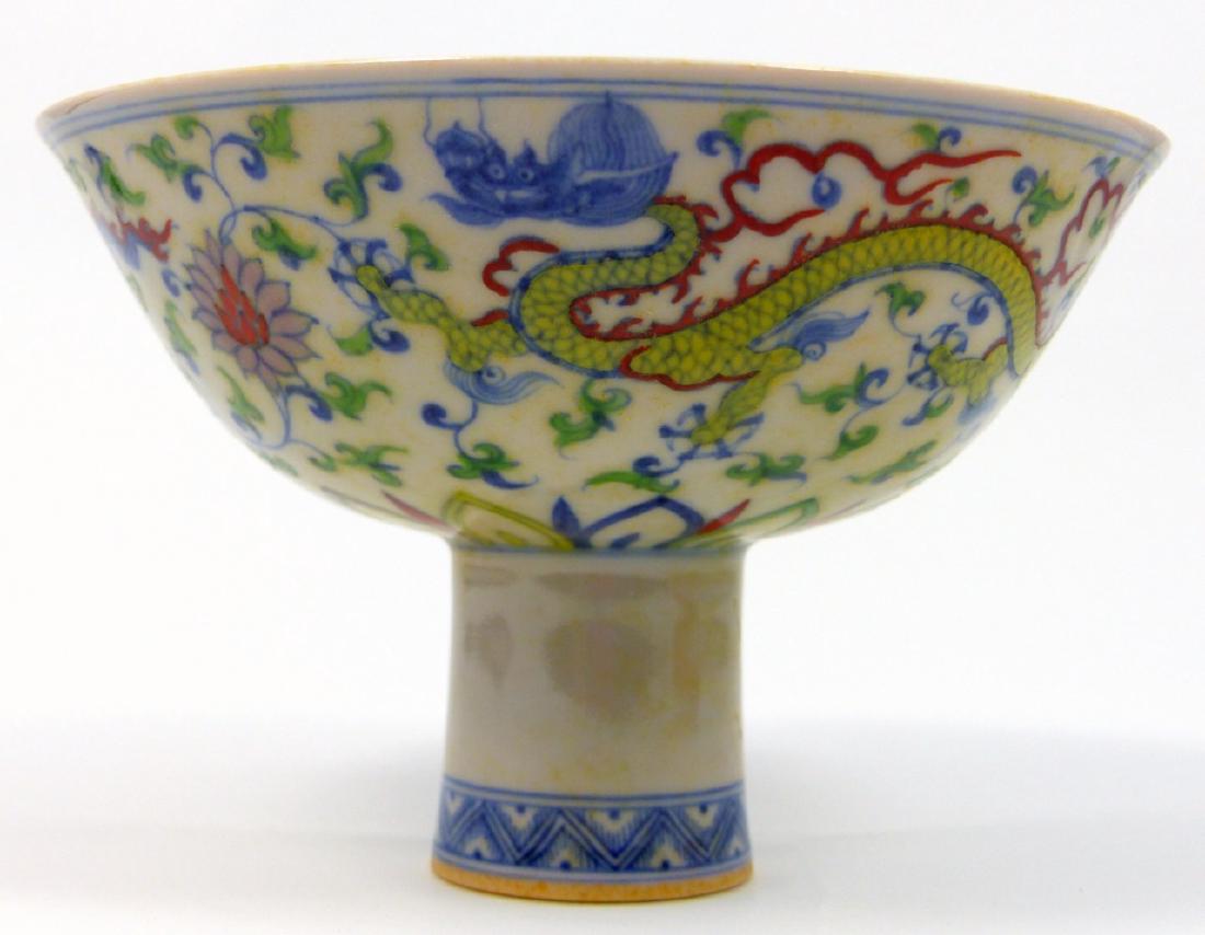 CHINESE WUCAI PORCELAIN STEM BOWL: Chinese Wucai porcelain stem bowl having dragons, stylized vines and floral blossoms to sides. Calligraphy marks to underside. Measures 6 1/8" (15.5cm) diameter.