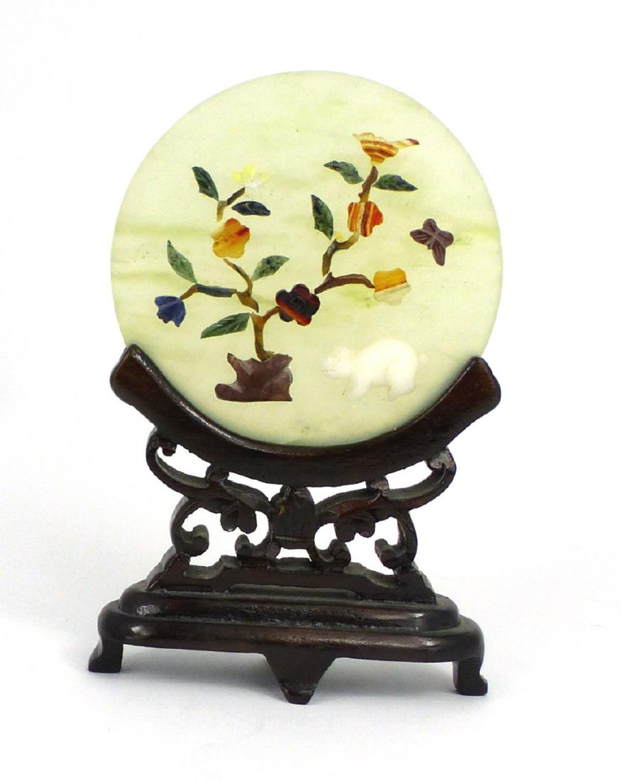 CHINESE JADE & SEMI-PRECIOUS STONE PLAQUE: Chinese jade and semi-precious stone round plaque on carved wood stand. Plaque measures 2 3/4" (7cm) diameter. Measures 4 1/2" (11.4cm) height overall.