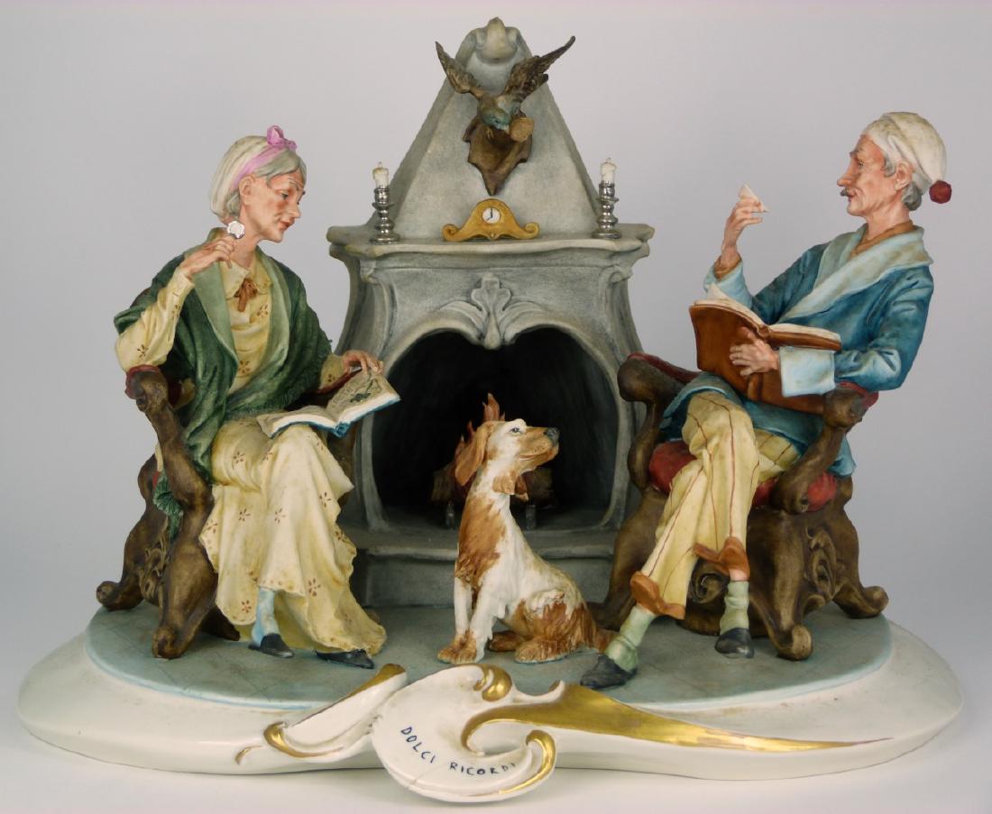 CAPODIMONTE DOLCI RICORDI FIGURAL PORCELAIN GROUP: Capodimonte porcelain grouping depicting a couple with dog seated around a fireplace. Titled 'Dolci Ricordi'. Holds crowned N mark to underside. Measures 13 1/2" (34.2cm) x 11" (28cm) x 10 1/2" (26.6c