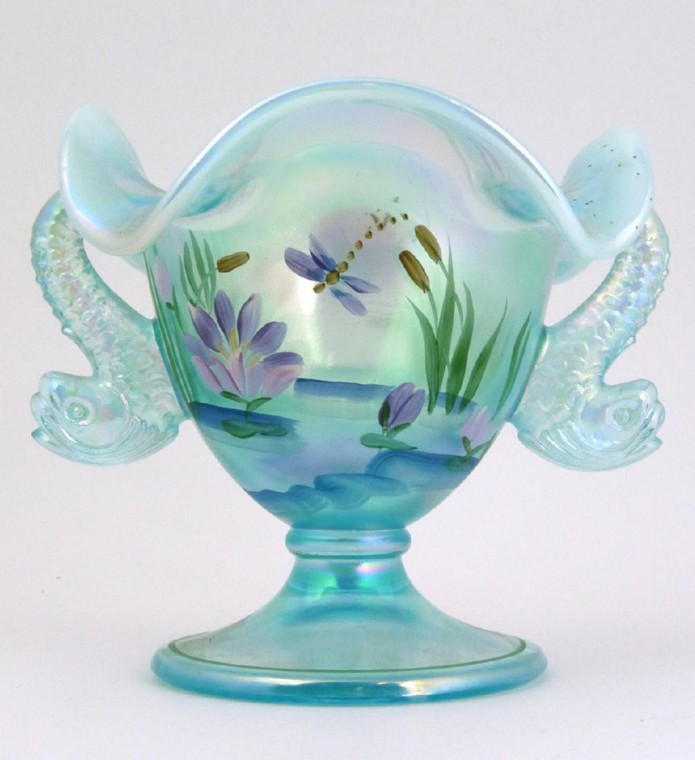 FENTON IRIDESCENT DOLPHIN HANDLED COMPOTE: Fenton iridescent footed bowl with pinched rim and dolphin handles. Marked to underside and inscribed Hand painted by Pam Heak. Holds original label to side. Measures 5 3/4" (14.6cm) height.