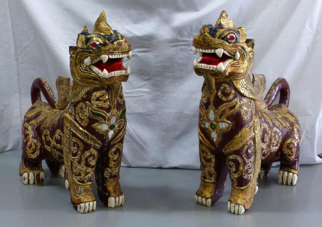 PR LARGE BALINESE POLYCHROME WOOD TEMPLE GUARDIANS: Pair of large Balinese carved and polychromed wooden foo lions. Each having inset glass "jewels" and gilt design to body. Each measures 35" (89cm) height and length.
