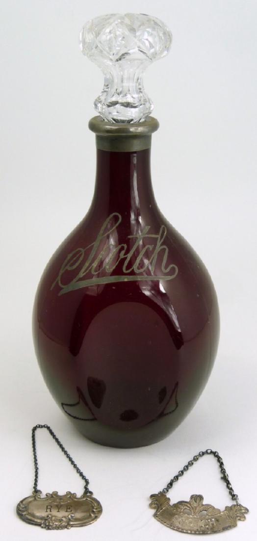 RUBY GLASS SCOTCH DECANTER w SILVER OVERLAY & TAGS: Ruby glass scotch decanter with silver overlay. Includes two sterling tags 'Scotch' and 'Rye' Each hallmarked and marked 925 or sterling. Measures 10 1/2" (26.5cm) height.
