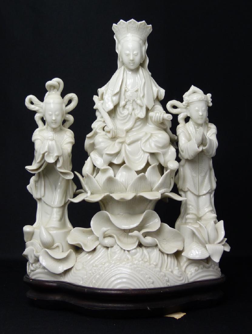 CHINESE BLANC DE CHINE BUDDHIST GROUP: Chinese blanc de chine porcelain figural group. Depicts Guanyin on lotus blossom with attendants. Measures 8 1/4" (21cm) height + 1" (2.5cm) wooden base.